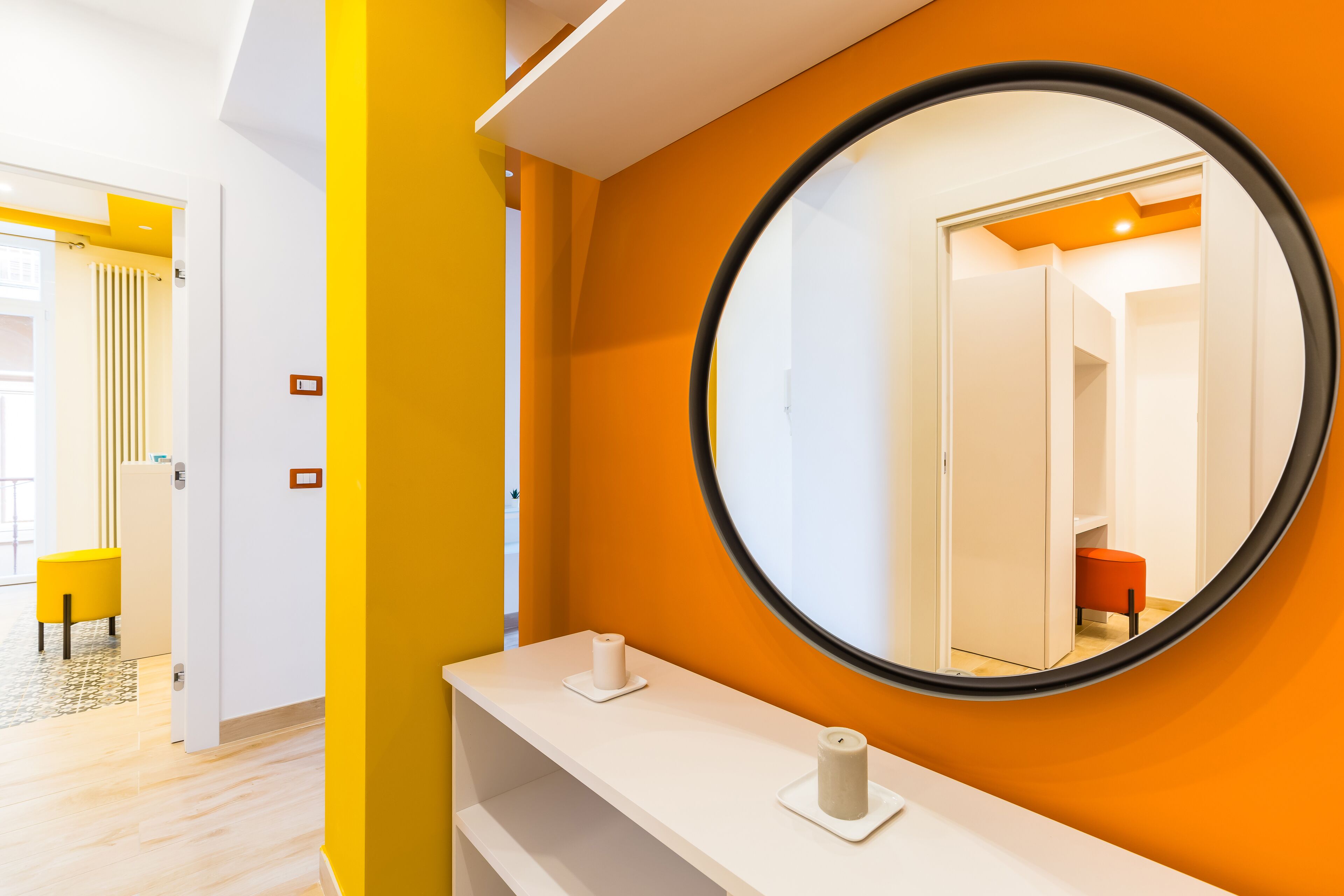 A bathroom with a round mirror, white vanity, and a yellow accent wall.