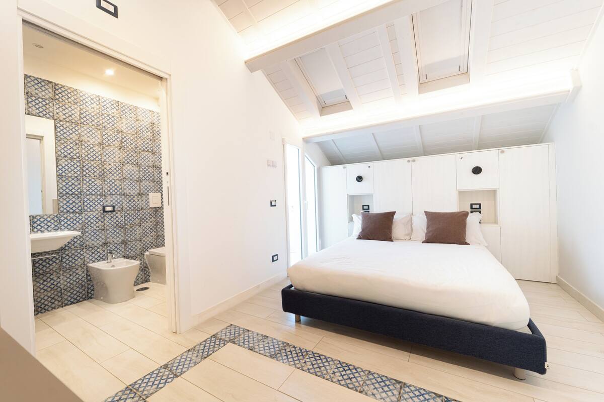 A bedroom with a bed, a bathroom with a sink and toilet, and a patterned floor.