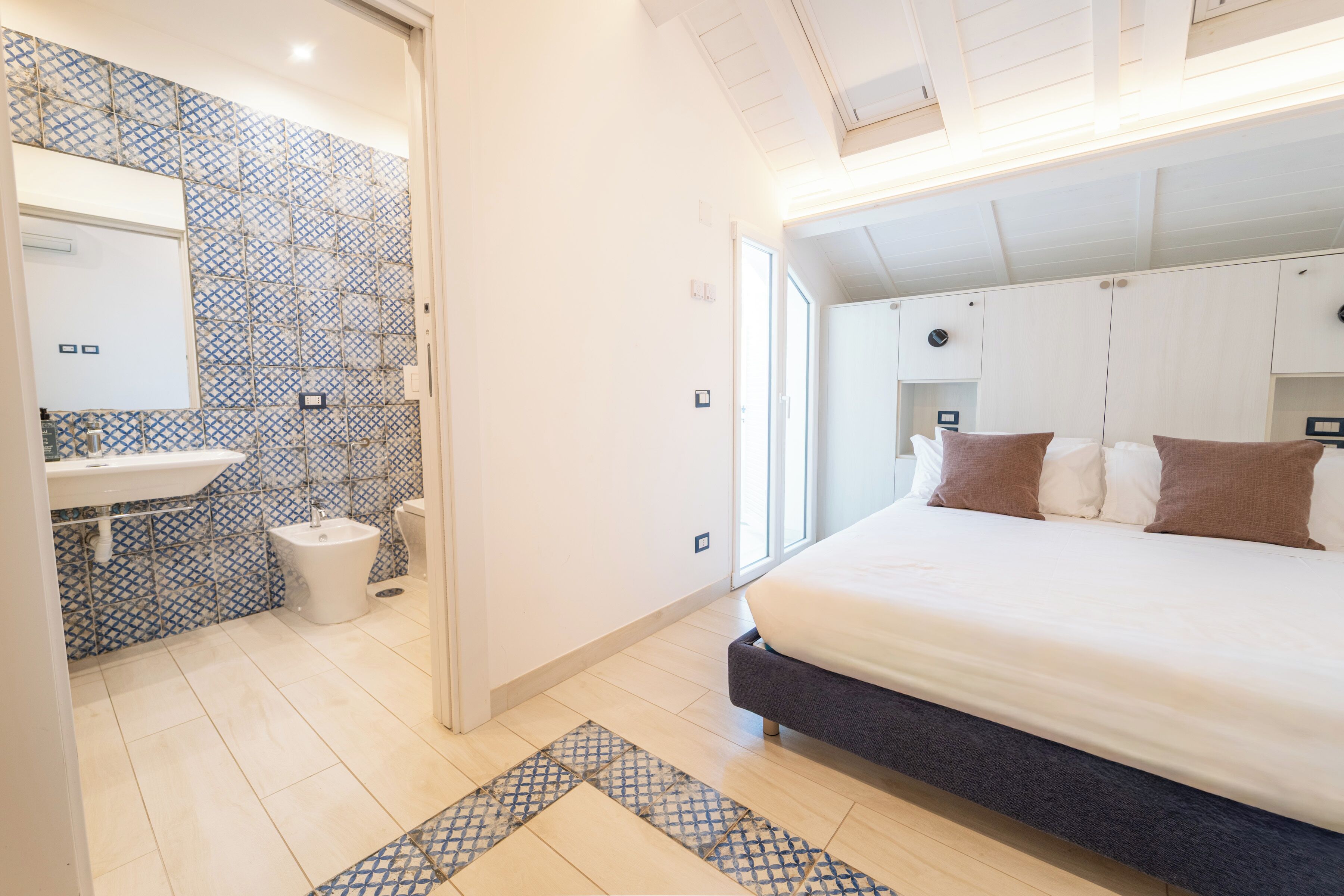A bedroom with a bed, a bathroom with a sink and toilet, and a patterned floor.