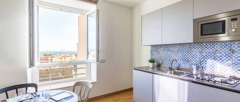 Una cocina moderna con un ventanal grande, una mesa de comedor preparada para cuatro personas y vistas a edificios.