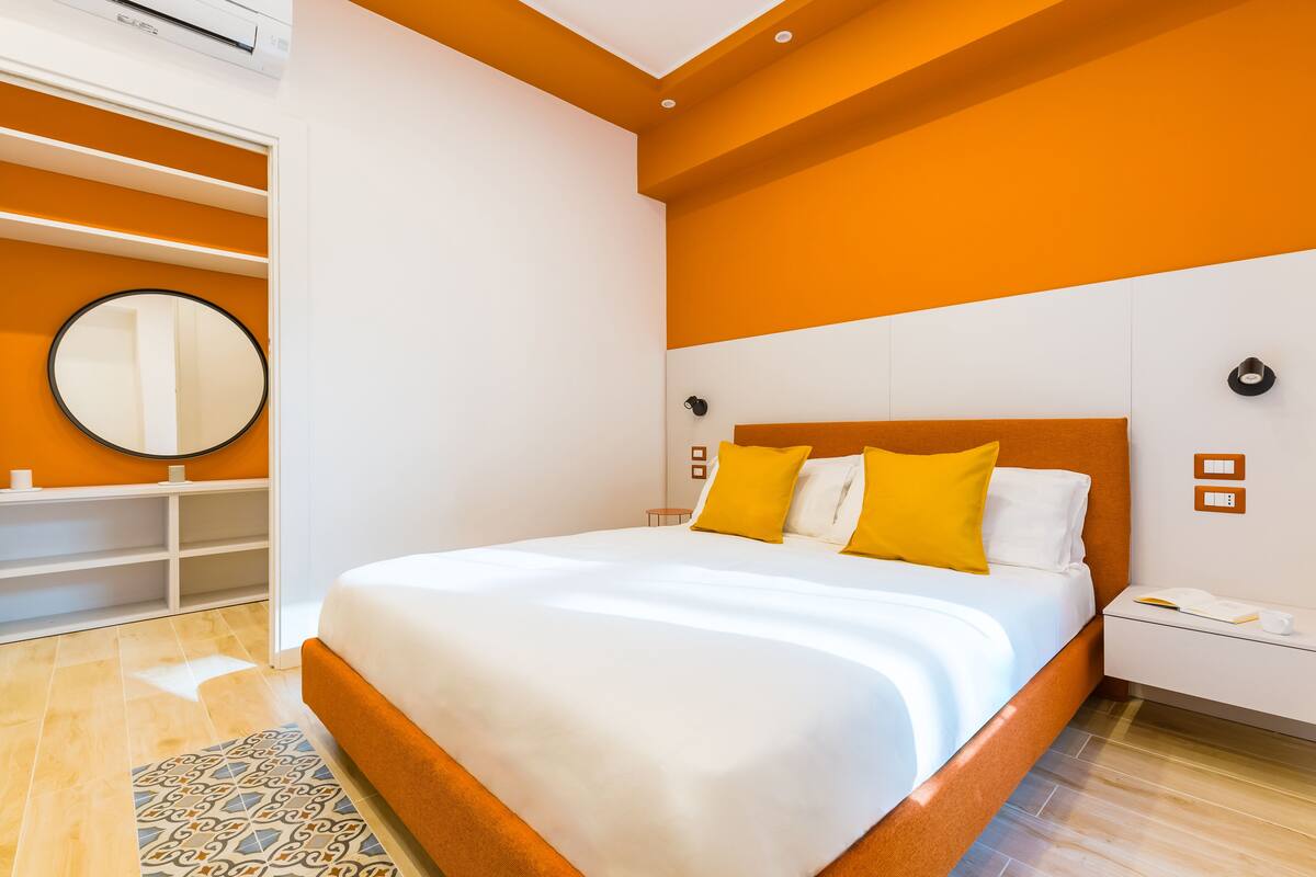 A modern hotel room with a large bed, a bedside table with a phone and a book, and a wardrobe with built-in shelves.