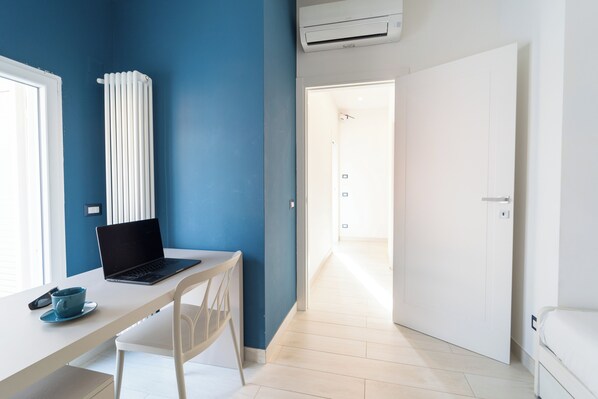 A room with a white desk, a laptop, a blue cup, a white chair, a radiator, and a white door. - Colonna Apartments by Wonderful Italy (Naples)