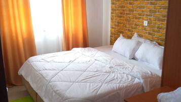 Una cama bien tendida con ropa blanca en una habitación con pared de ladrillo y alfombra verde.