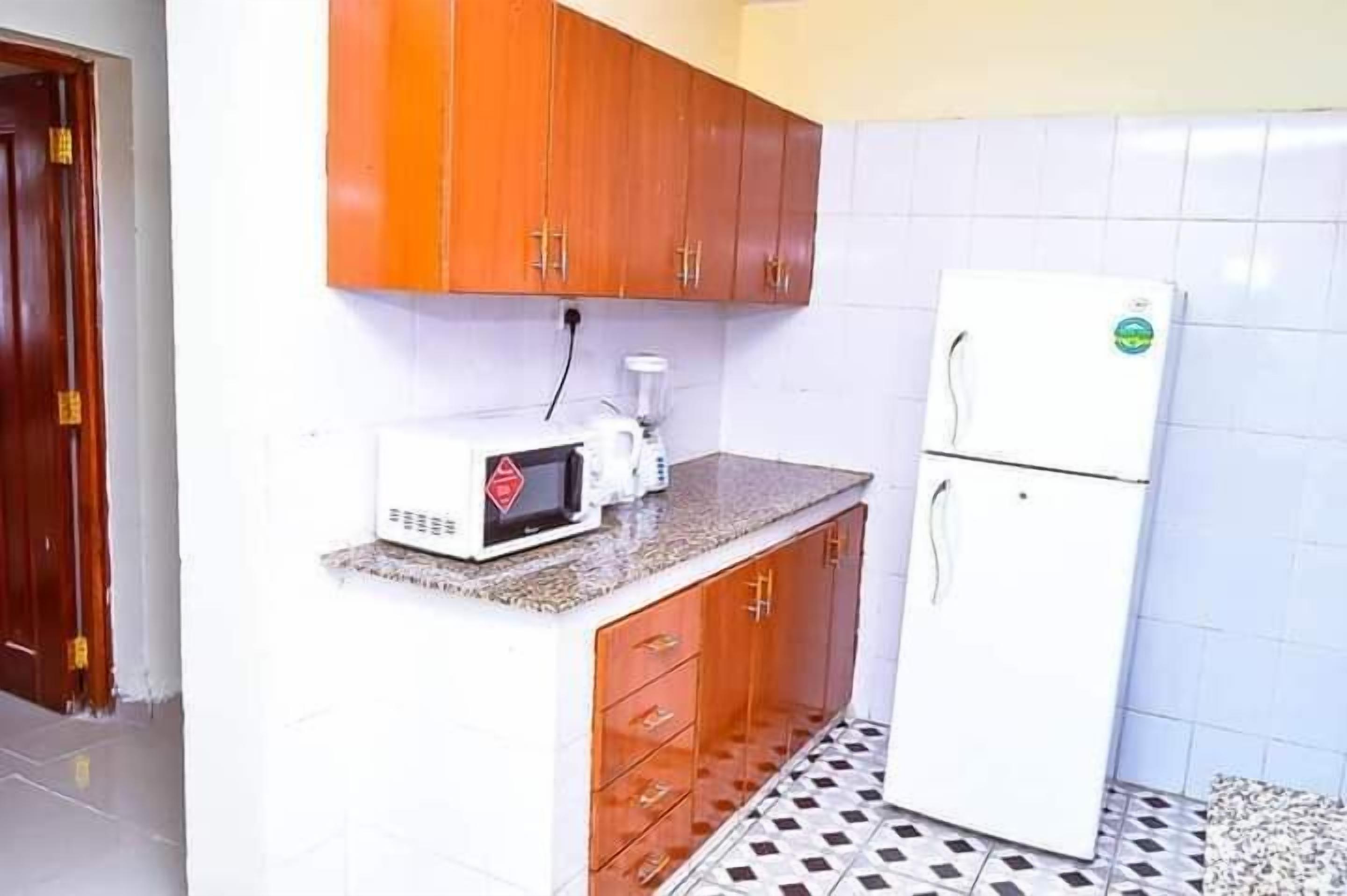 Eine Küche mit Holzausstattung, einer Mikrowelle, einem Kühlschrank und einem gefliesten Boden.