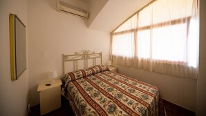 A bedroom with a bed, a nightstand, a lamp, an air conditioner, and a window with curtains.