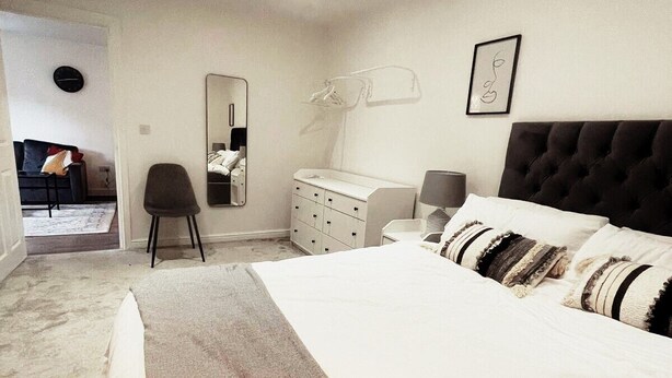 A bedroom with a large bed, a dresser, a chair, a mirror, and a clock on the wall. - City Centre Luxury apartment (Cardiff)