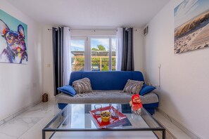 Ein Wohnzimmer mit einem blauen Sofa, einem Glastisch mit Snacks und einem Hundebild an der Wand.