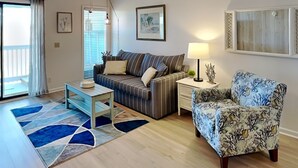 A living room with a sofa, a patterned armchair, a coffee table, a lamp, and a ceiling fan. - A Place at the Beach | Easy Walk to the Sand + Community Pool! (Carolina Beach)