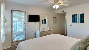 A bedroom with a bed, a dresser, a television, a ceiling fan, and a window with blinds. - A Place at the Beach | Easy Walk to the Sand + Community Pool! (Carolina Beach)