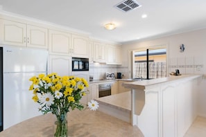 A kitchen with white cabinets, a built-in oven, a refrigerator, and a window with curtains. - 71 Blanche Pde Hindmarsh Island (Hindmarsh Island)