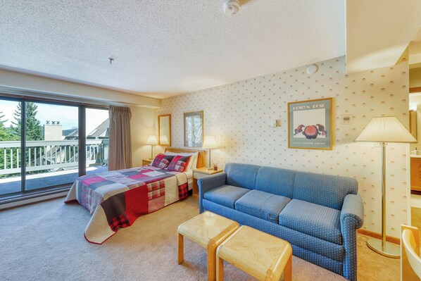 A hotel room with a bed, a blue sofa, a wooden coffee table, and a large window offering a view of the outdoors. - Mountain Green (Killington)