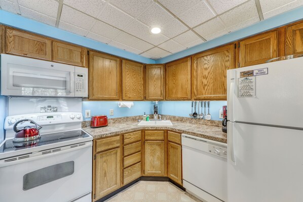 A kitchen with wooden cabinets, a white microwave, stove, and refrigerator.