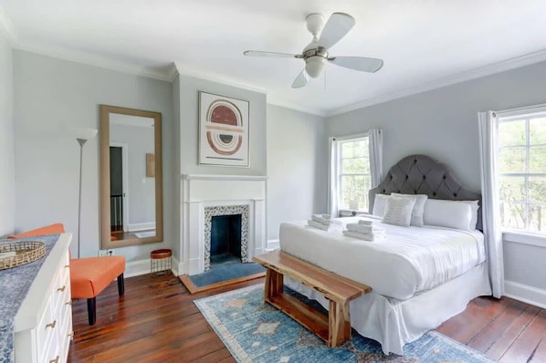 A bedroom with a large bed, a fireplace, a ceiling fan, and a window with a view.