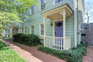 A light green two-story house with a purple front door, white porch columns, and a brick pathway.