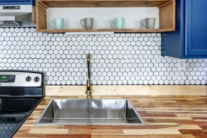 A kitchen with a stainless steel sink, wooden countertop, and a hexagonal tile backsplash.