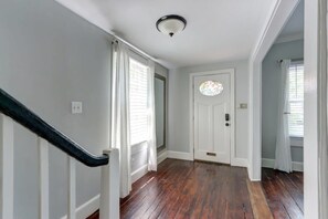A hallway with wooden flooring, white walls, a black handrail, and a door with a stained glass window.