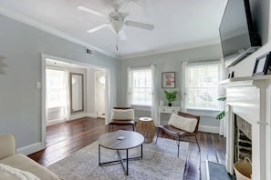 A spacious living room with hardwood flooring, a ceiling fan, a fireplace, and a television.