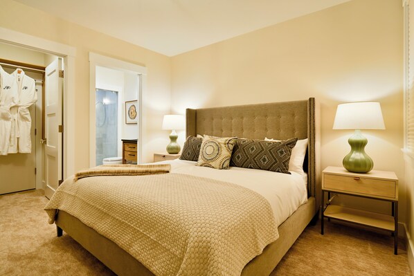 A hotel room with a large bed, two bedside tables, a wardrobe, and a bathroom visible through an open door.