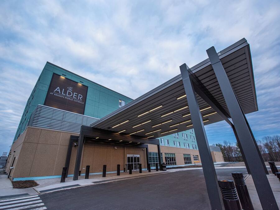 A modern hotel entrance with a prominent sign, a covered walkway, and a clear sky.