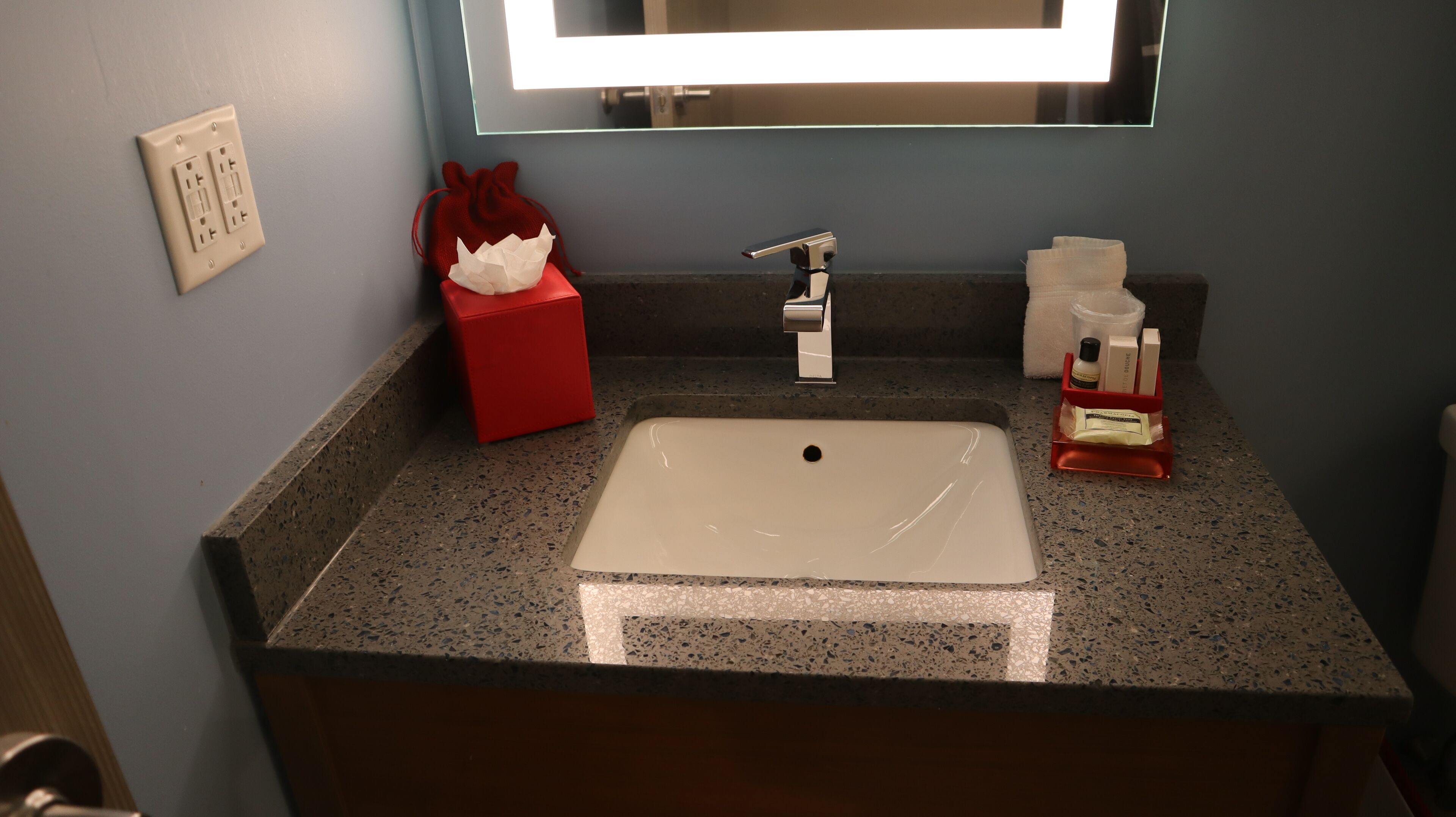 A bathroom with a white sink, a mirror, a red tissue box, and toiletries on the counter.