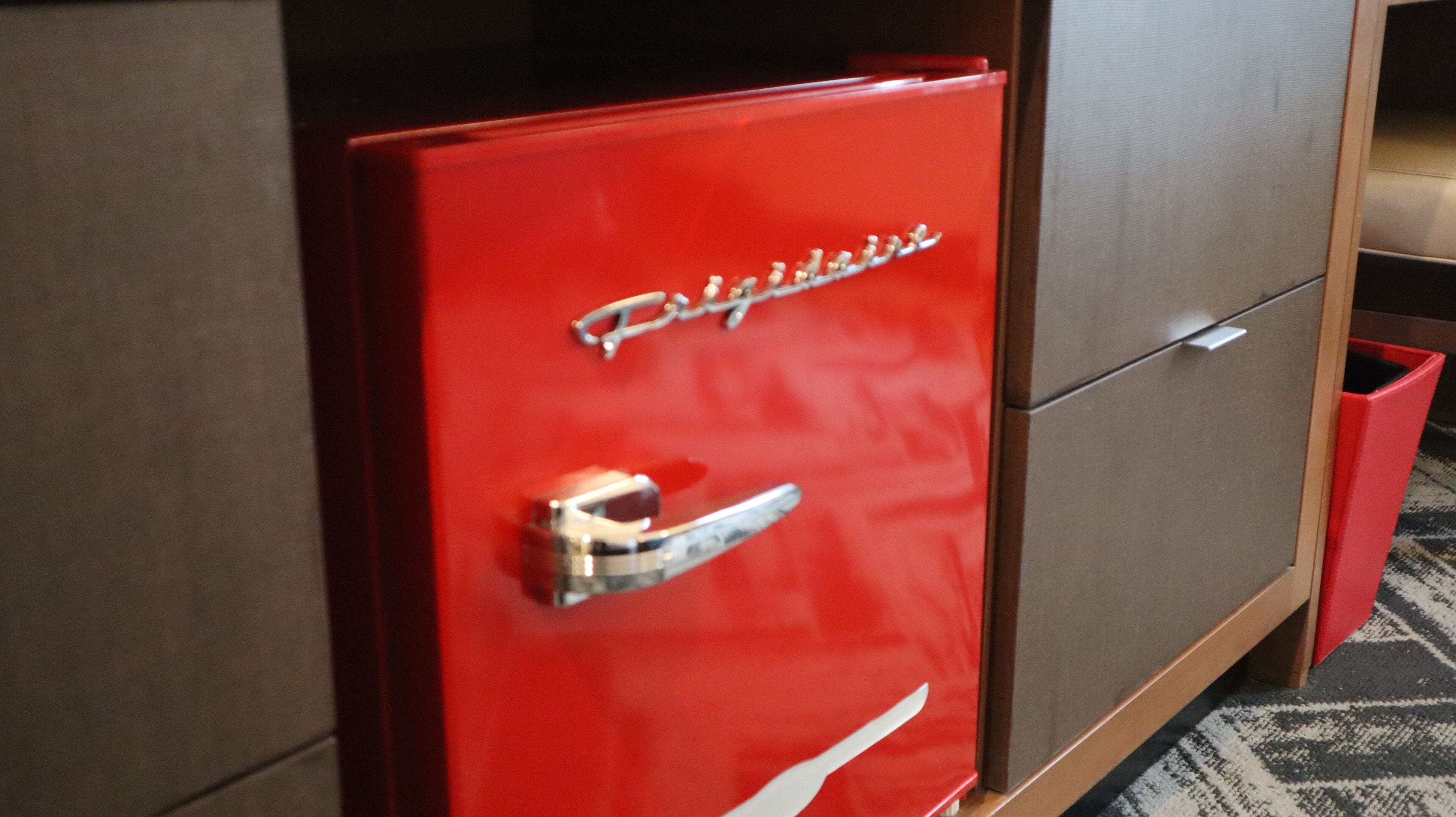 A red filing cabinet with a handle and a drawer, part of a wooden cabinet structure.