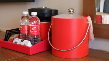 Un minibar rojo con una botella de agua, una botella de jugo y un recipiente negro, posiblemente una cafetera, sobre una superficie de madera.