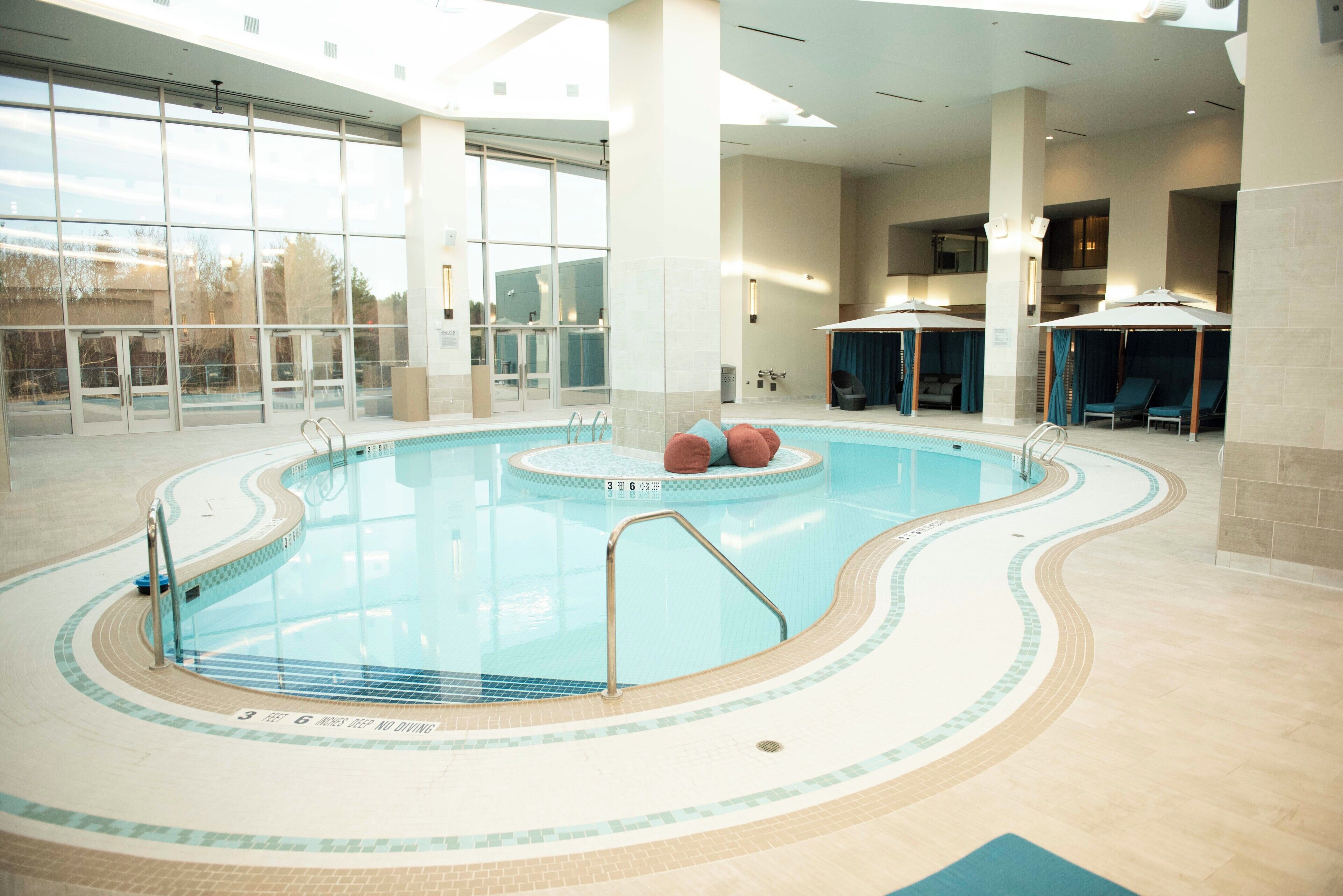 Una piscina interior con agua cristalina, suelo de baldosas y algunas tumbonas.
