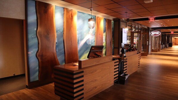 Un mostrador de recepción con diseño de madera y una pantalla digital, un letrero de Monster Golf Club y un letrero de salida.