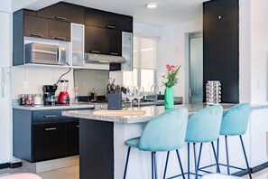 A modern kitchen with dark cabinets, a stainless steel range hood, a granite countertop, and a central island with bar stools.