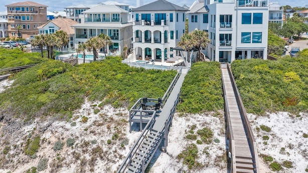 A coastal property with a modern architectural style, featuring a large pool area, multiple balconies, and a wooden boardwalk leading to a sandy beach.