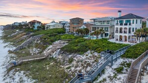 A coastal residential area with multiple houses, a wooden staircase leading down to the beach, and a clear view of the ocean.