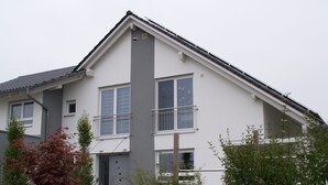 A modern two-story residential building with a grey facade, white trim, and a sloped roof.
