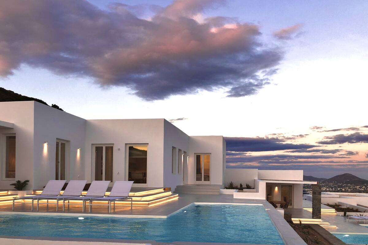 A modern poolside area with lounge chairs and a pool, surrounded by a white building with large windows and a view of the landscape.