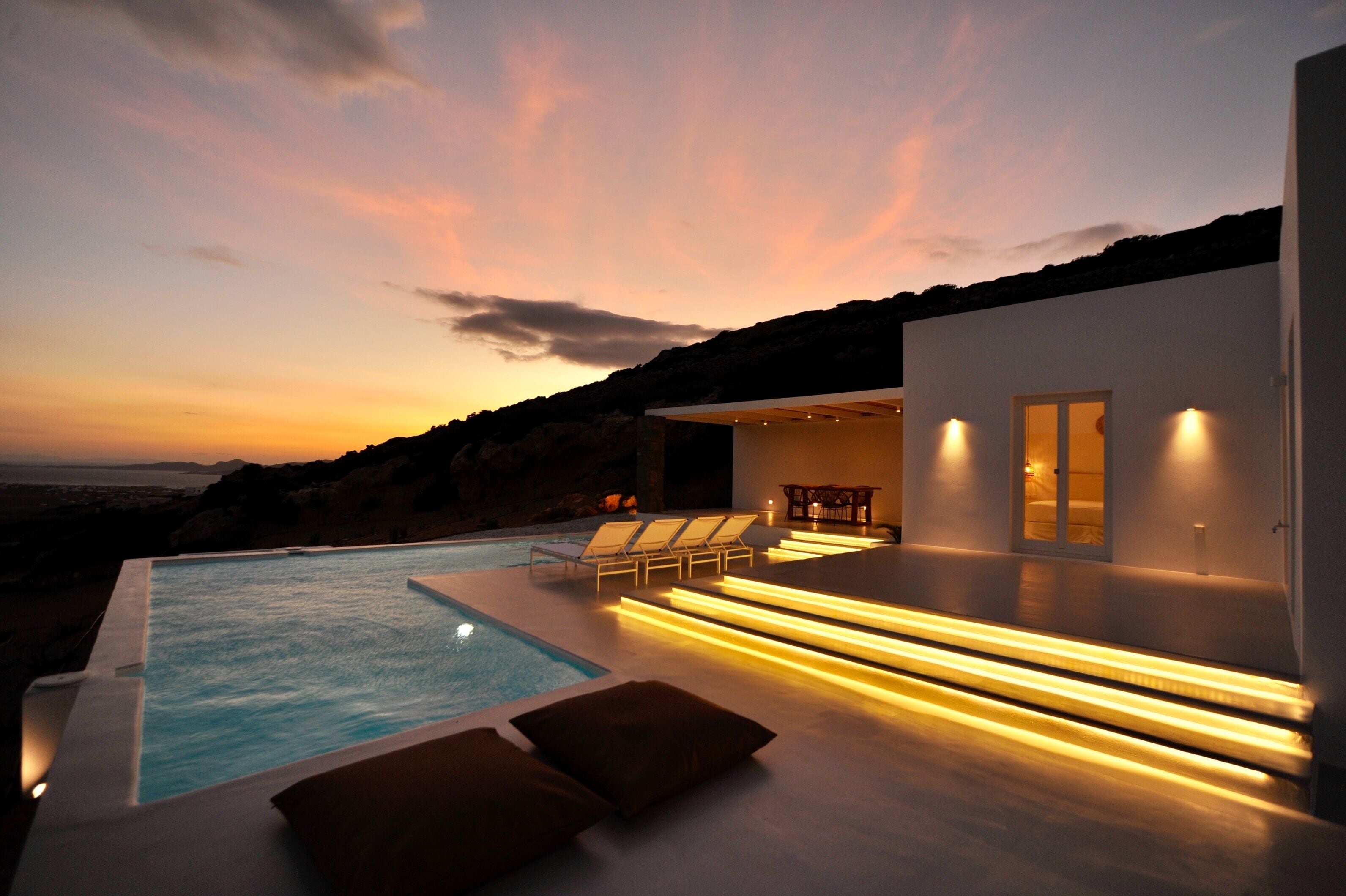 A modern outdoor pool area with lounge chairs and a sunset view.