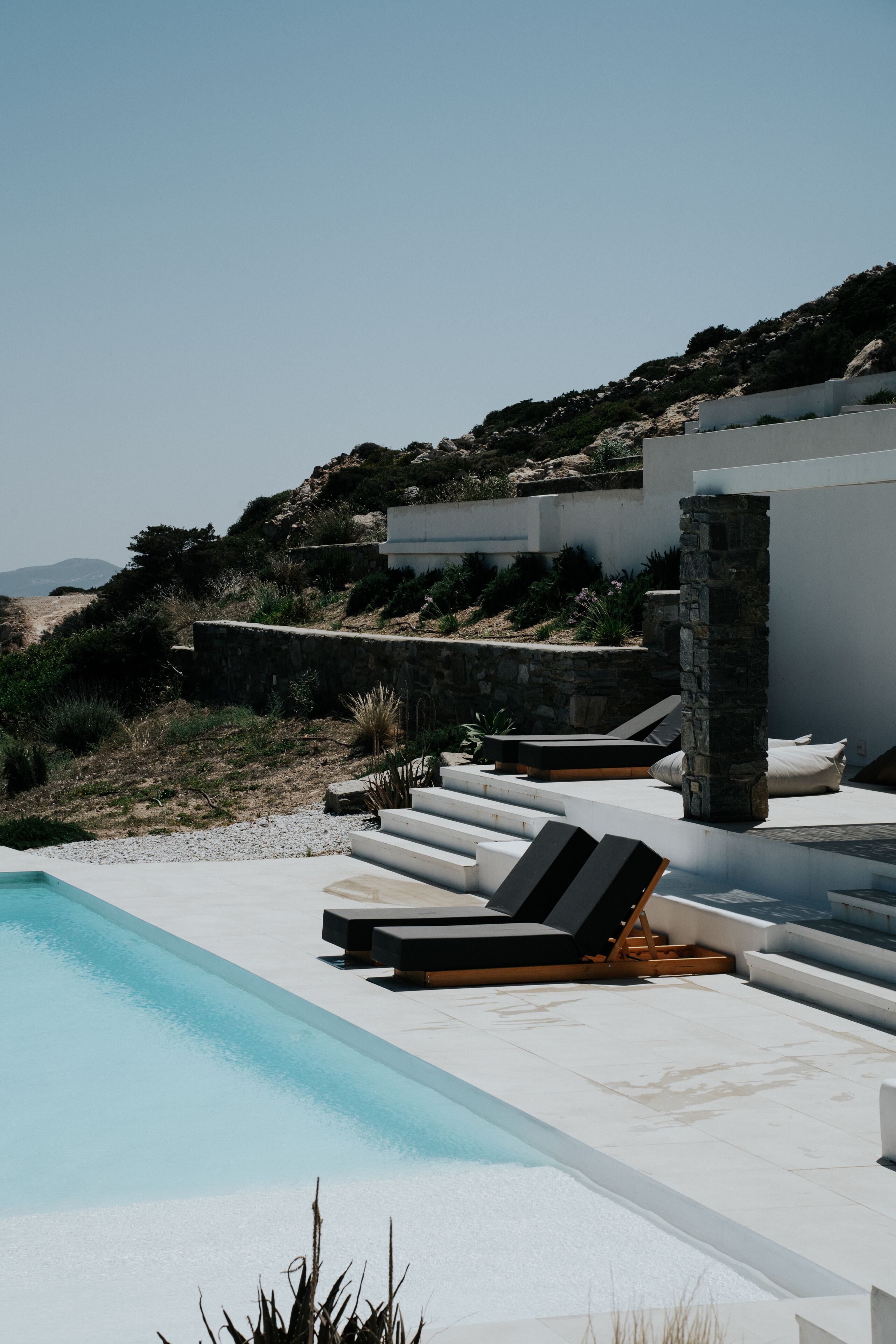 A pool area with lounge chairs and a stone pillar.