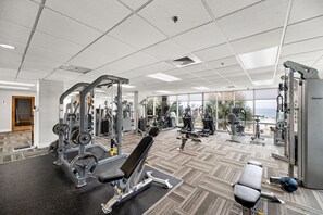 A gym with various exercise equipment, large windows, and a view of the ocean.