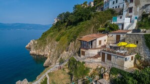 Una propiedad costera con fachada de piedra, un balcón con sombrillas amarillas y vistas al mar.