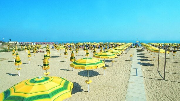 A beach with rows of yellow and green striped umbrellas and a clear blue sky. - Ferienpark Cesenatico Mobilehome Riviera für 6 Personen (Cesenatico)