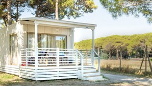 Eine kleine, eingeschossige Hütte mit einer Veranda und einem überdachten Eingang, umgeben von Bäumen und einer Rasenfläche.