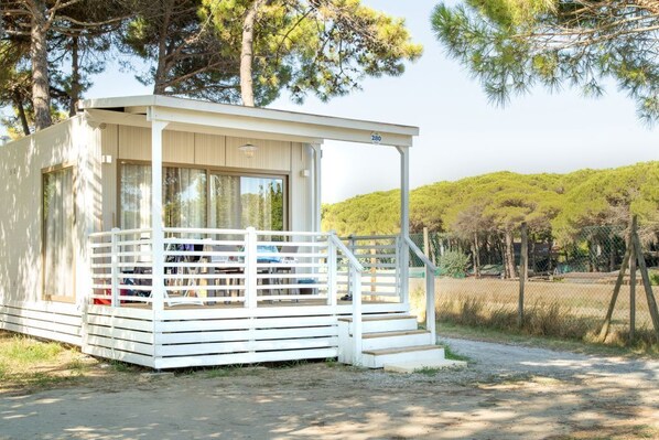 Une petite cabane à un seul étage, dotée d’un porche et d’une entrée couverte, entourée d’arbres et d’une zone herbeuse.