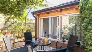 An outdoor patio with wicker chairs and a table, a wooden building with a glass door, and a garden with potted plants. - Lovely apartment DESIREE in Rovinj (Rovinj)