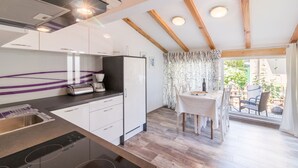 A modern kitchen with white cabinets, a built-in oven, and a coffee maker. There is a dining area with a table and chairs, and a view of the outdoors through a window with curtains. - Lovely apartment DESIREE in Rovinj (Rovinj)