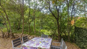 An outdoor patio with a table covered in a floral tablecloth, surrounded by metal chairs.