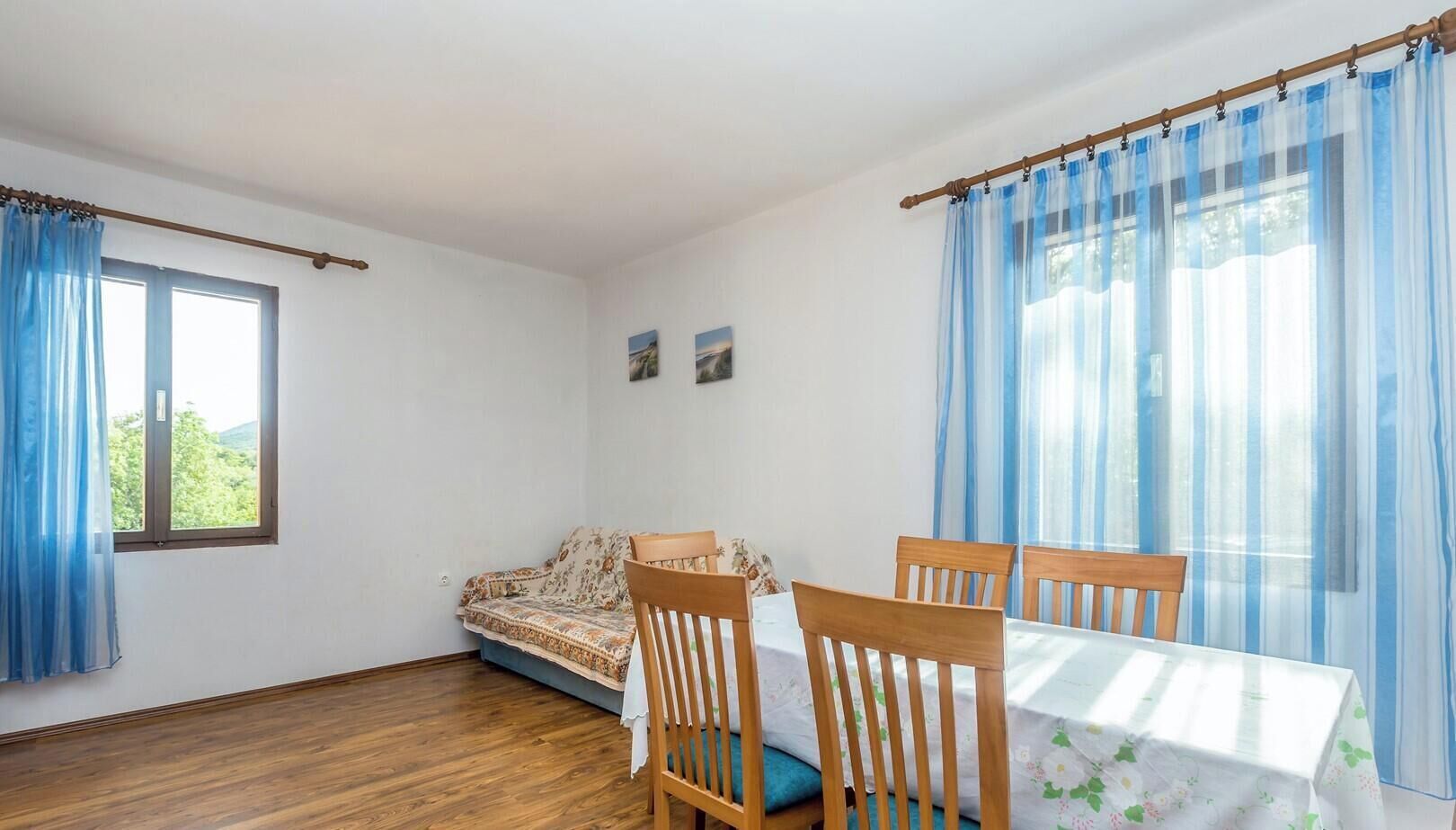 Una habitación con sofá, una mesa de comedor con sillas, una ventana con cortinas e imagen colgada en la pared.