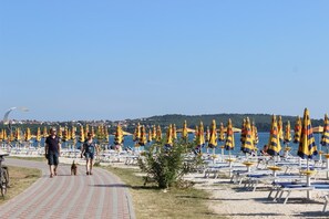 Stroll along the beachside promenade to a sandy beach area with shaded seating and lounge chairs.