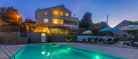 Ein modernes, zweistöckiges Haus mit Swimmingpool, Außenbereich zum Sitzen und einer gut beleuchteten Eingangsparte.