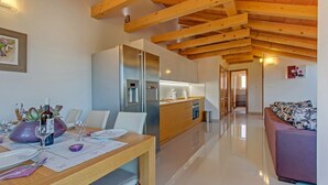 A modern kitchen with wooden beams, stainless steel appliances, and a dining area with a table set for two. - Apartment ROSE with large heated pool 50m2 and sea view (Nerezine)