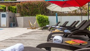 A poolside area with lounge chairs, a red umbrella, and a small garden. - Apartment ROSE with large heated pool 50m2 and sea view (Nerezine)