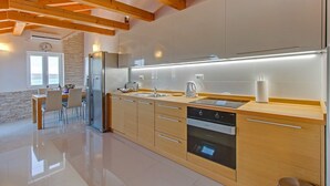 A modern kitchen with wooden beams, a built-in oven, and a dining area with a table and chairs. - Apartment ROSE with large heated pool 50m2 and sea view (Nerezine)