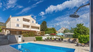 A swimming pool with a showerhead, lounge chairs, and umbrellas. - Apartment ROSE with large heated pool 50m2 and sea view (Nerezine)